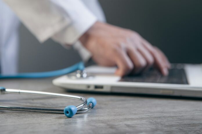 Doctor typing on a laptop with a stethoscope nearby.